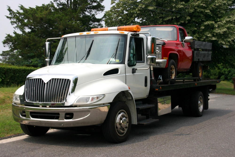 A tow truck stands ready on the roadside, its powerful frame adorned with a bright amber alert light. 