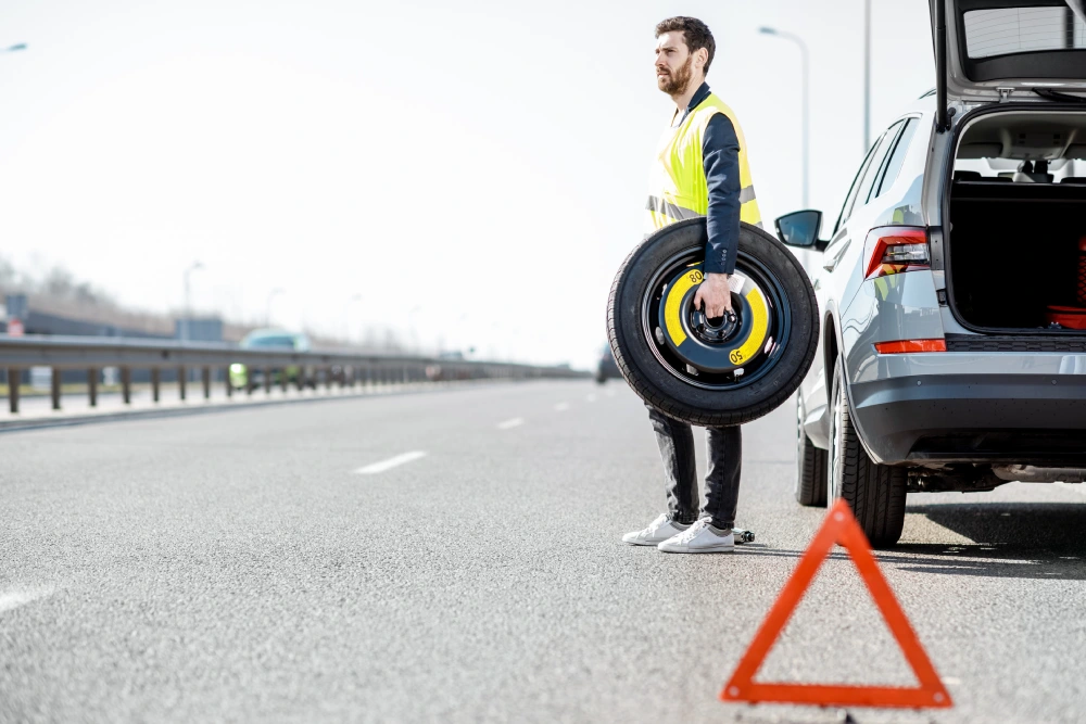 Man changing wheel standing with spare wheel near the broken car on the roadside